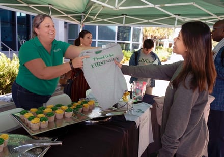 A staff member gives a first-gen shirt to a student.
